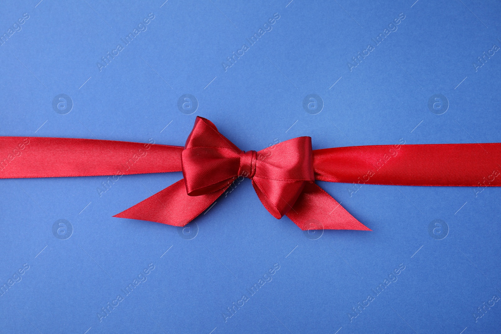 Photo of Red satin ribbon with bow on blue background, top view