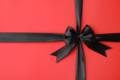Black satin ribbon with bow on red background, top view