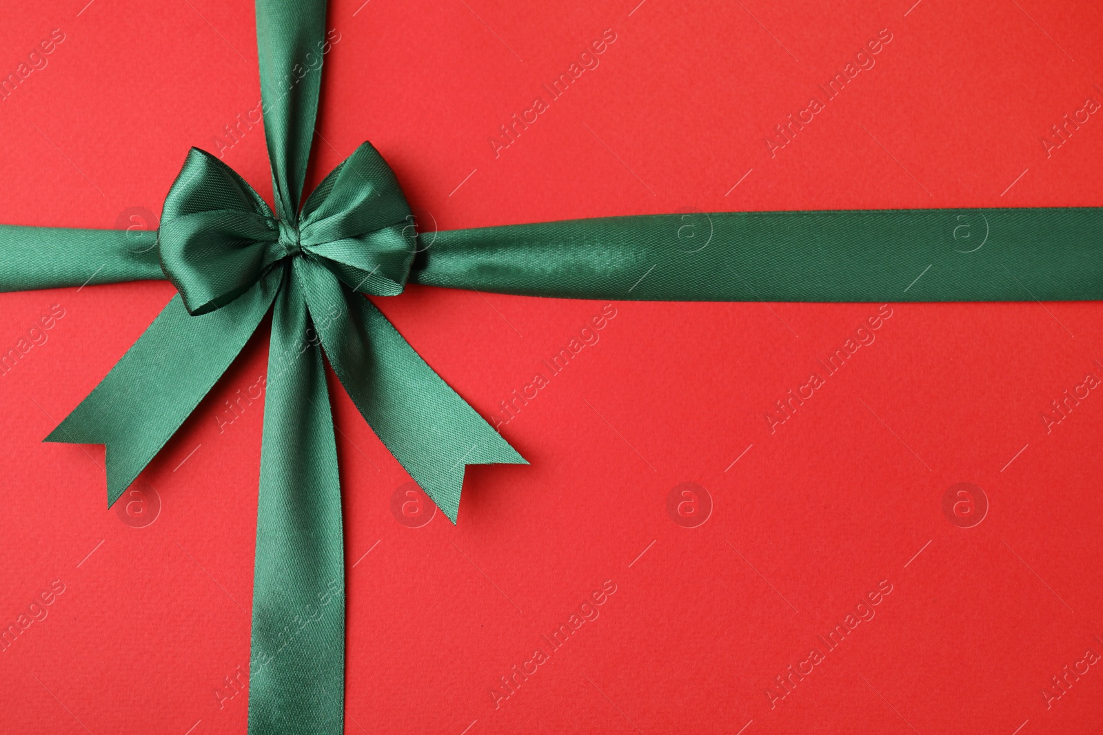 Photo of Green satin ribbon with bow on red background, top view