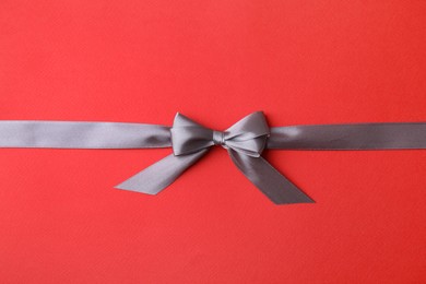 Grey satin ribbon with bow on red background, top view