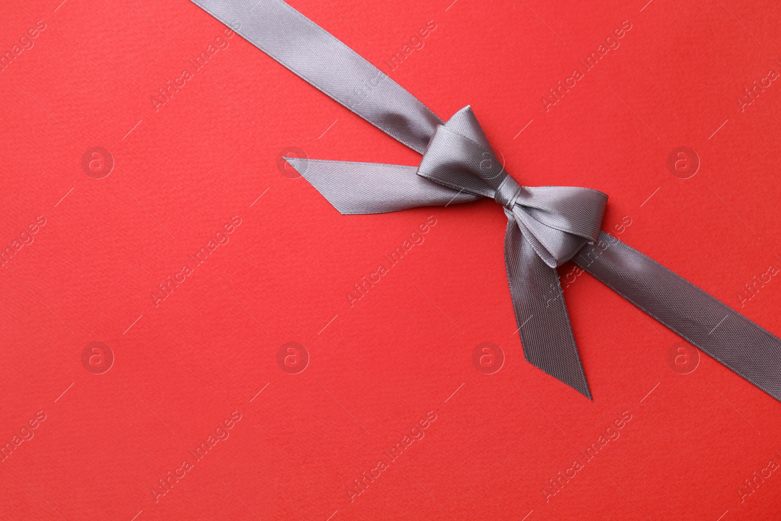 Photo of Grey satin ribbon with bow on red background, top view. Space for text