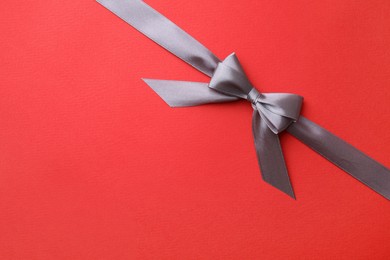 Photo of Grey satin ribbon with bow on red background, top view. Space for text