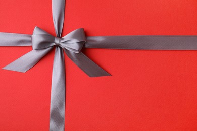 Photo of Grey satin ribbon with bow on red background, top view