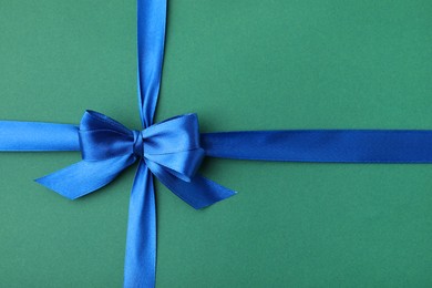 Photo of Blue satin ribbon with bow on green background, top view