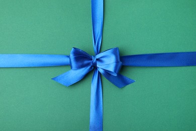 Blue satin ribbon with bow on green background, top view