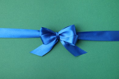 Blue satin ribbon with bow on green background, top view