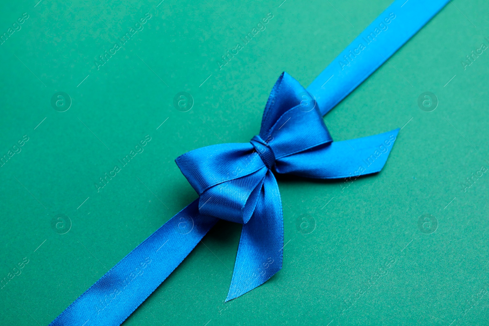 Photo of Blue satin ribbon with bow on green background