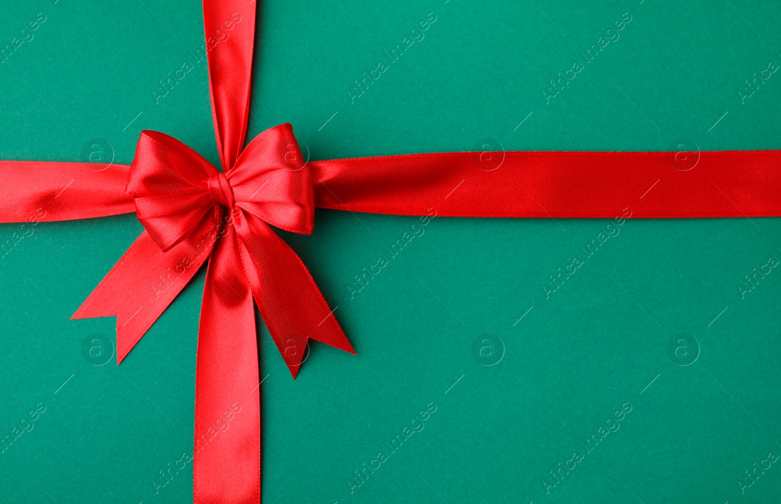 Photo of Red satin ribbon with bow on green background, top view