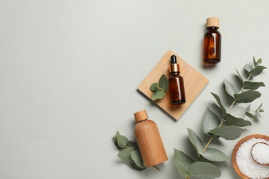 Aromatherapy products. Bottles of essential oil, sea salt and eucalyptus leaves on grey background, flat lay. Space for text