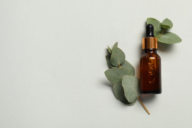 Photo of Aromatherapy product. Bottle of essential oil and eucalyptus leaves on grey background, flat lay. Space for text