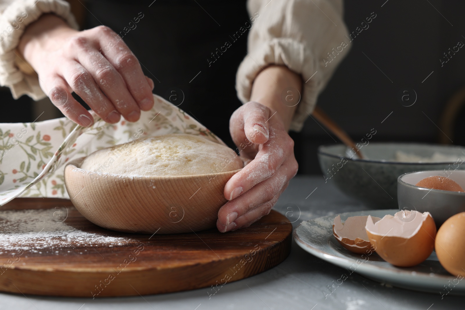 Photo of Woman covering dough with napkin at grey table, closeup