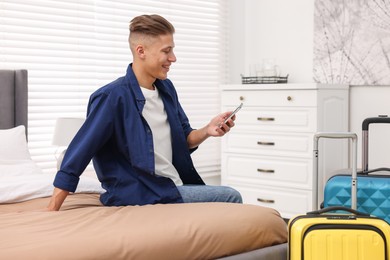 Photo of Smiling guest with smartphone on bed in stylish hotel room