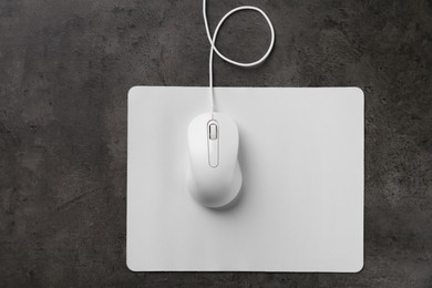 Photo of Wired mouse with mousepad on black textured table, top view. Space for text