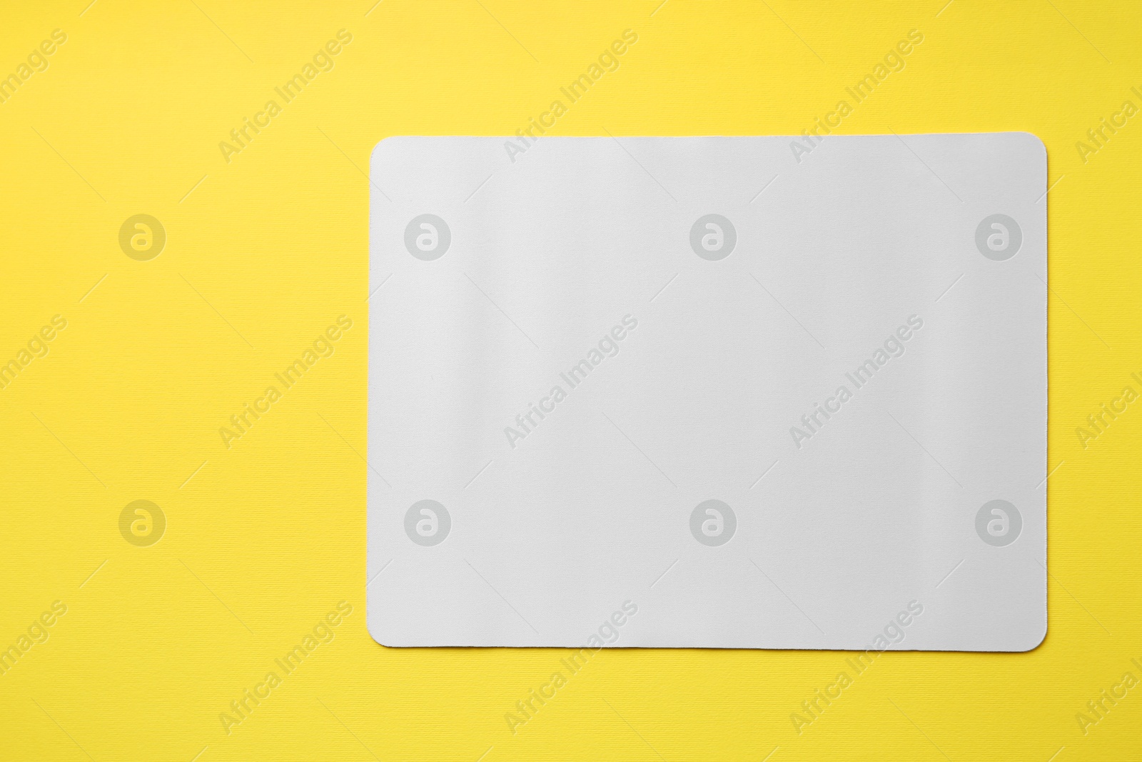 Photo of One white mouse pad on yellow background, top view. Space for text