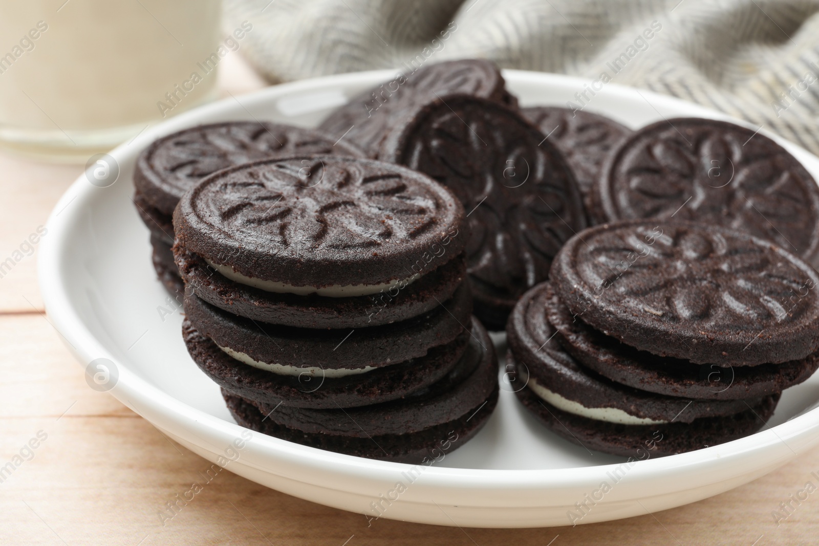 Photo of Plate with tasty sandwich cookies on light wooden table, closeup