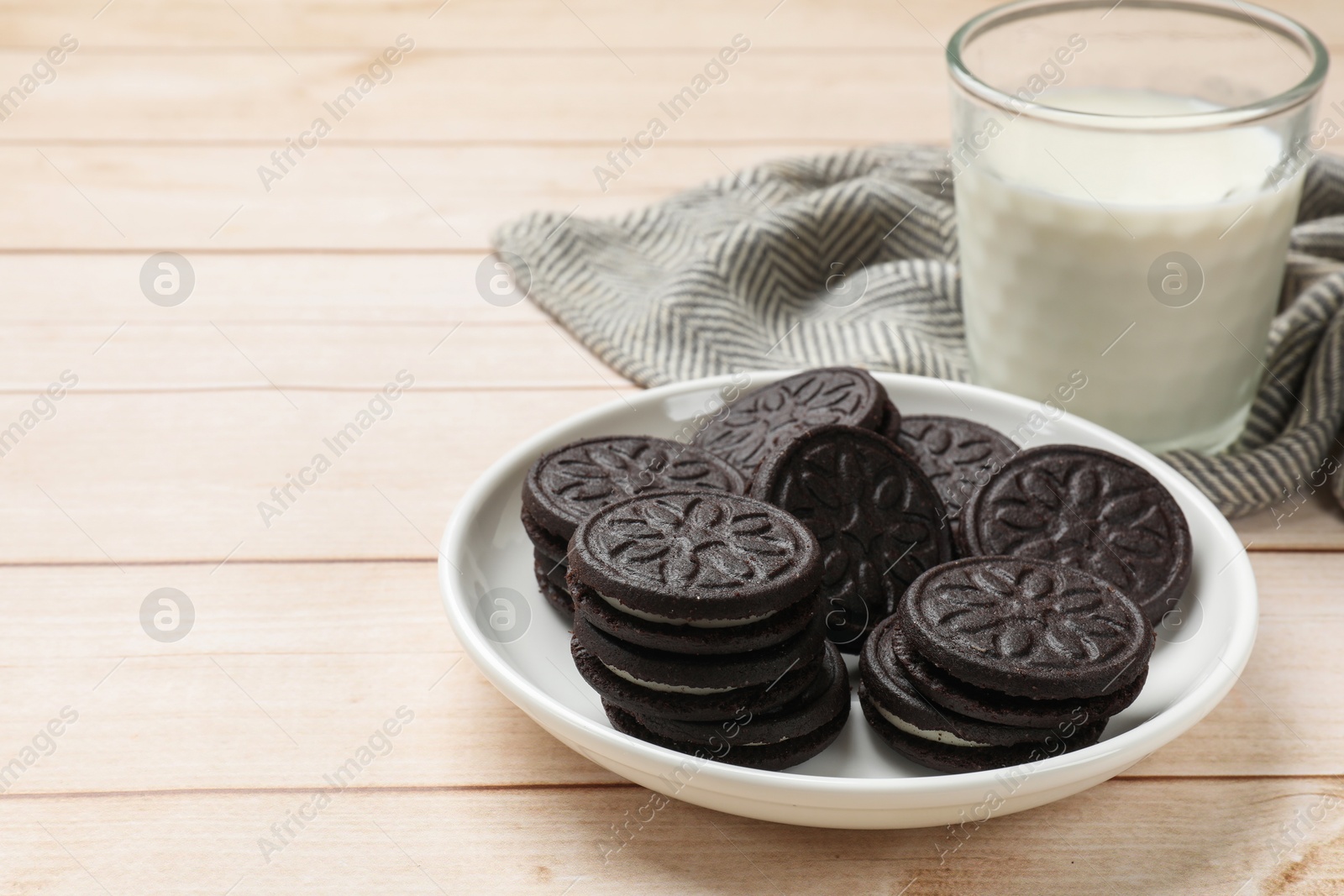 Photo of Plate with tasty sandwich cookies and milk on light wooden table, closeup. Space for text