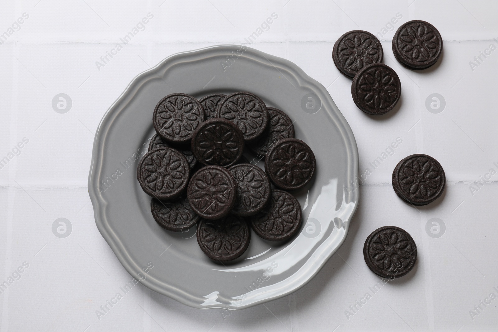 Photo of Plate with tasty sandwich cookies on white tiled table, flat lay