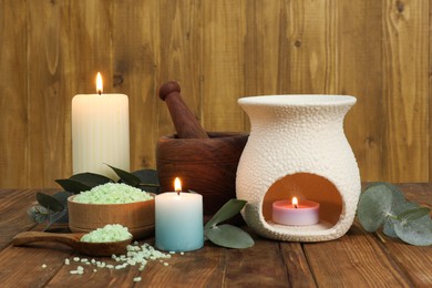 Aromatherapy products, burning candles and eucalyptus leaves on wooden table