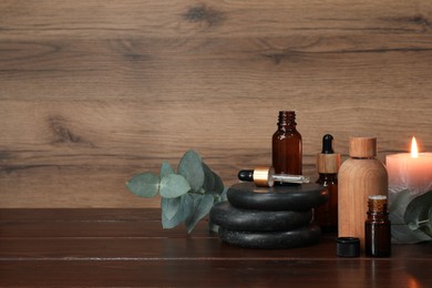 Aromatherapy products and burning candle on wooden table, space for text