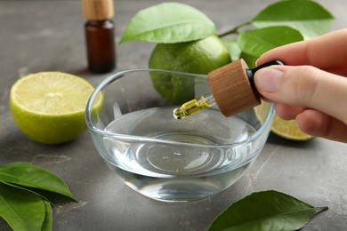 Woman dripping essential oil from pipette into bowl at gray table, closeup