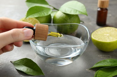 Woman dripping essential oil from pipette into bowl at gray table, closeup