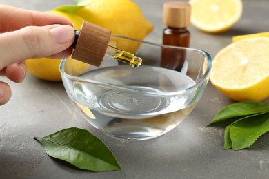 Woman dripping essential oil from pipette into bowl at gray table, closeup