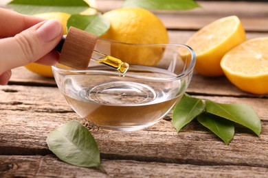 Woman dripping essential oil from pipette into bowl at wooden table, closeup