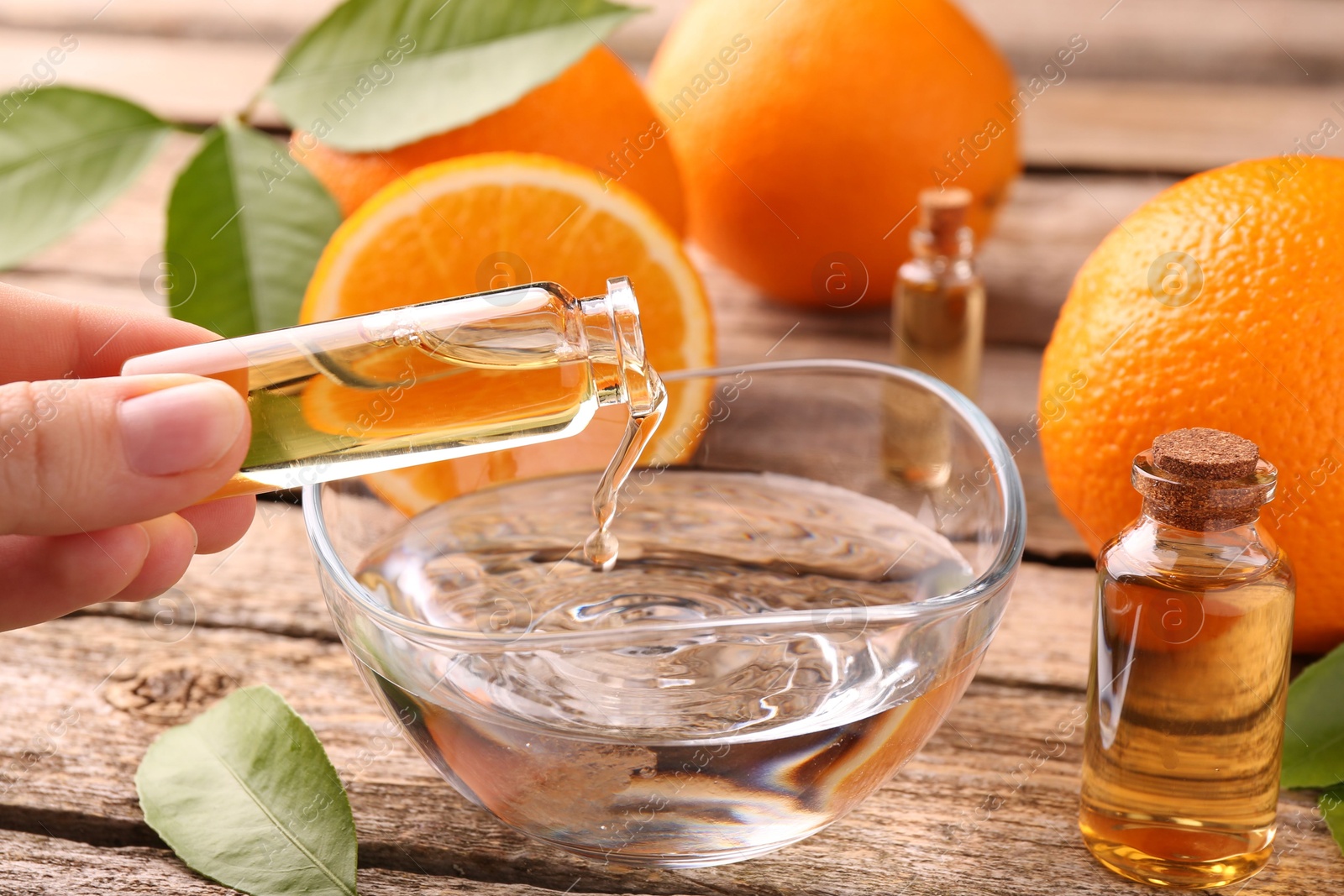 Photo of Woman pouring essential oil from cosmetic bottle into bowl at wooden table, closeup