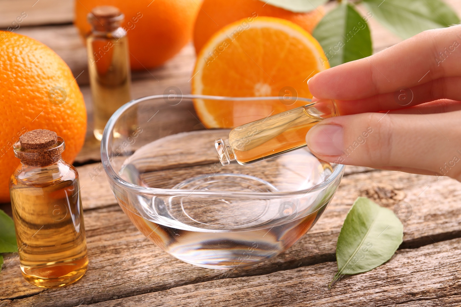 Photo of Woman pouring essential oil from cosmetic bottle into bowl at wooden table, closeup