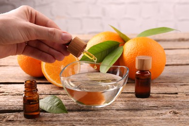 Photo of Woman pouring essential oil from cosmetic bottle into bowl at wooden table, closeup