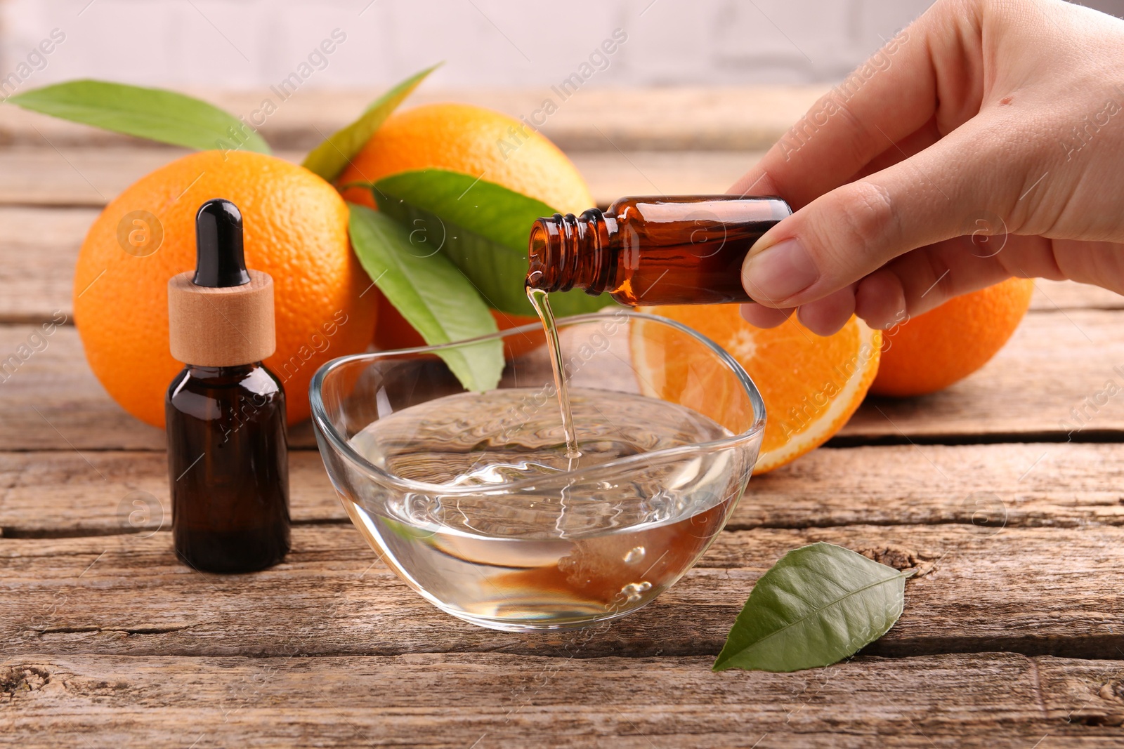 Photo of Woman pouring essential oil from cosmetic bottle into bowl at wooden table, closeup