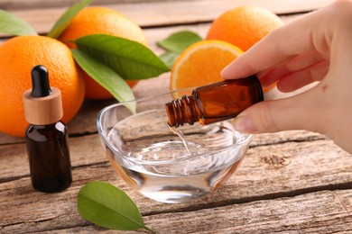 Photo of Woman pouring essential oil from cosmetic bottle into bowl at wooden table, closeup