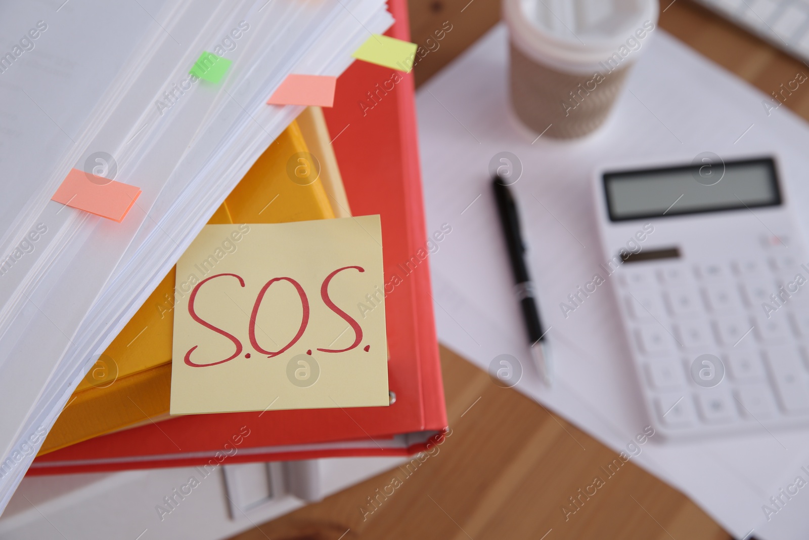 Photo of Note with word SOS and stationery on wooden table at workplace, closeup