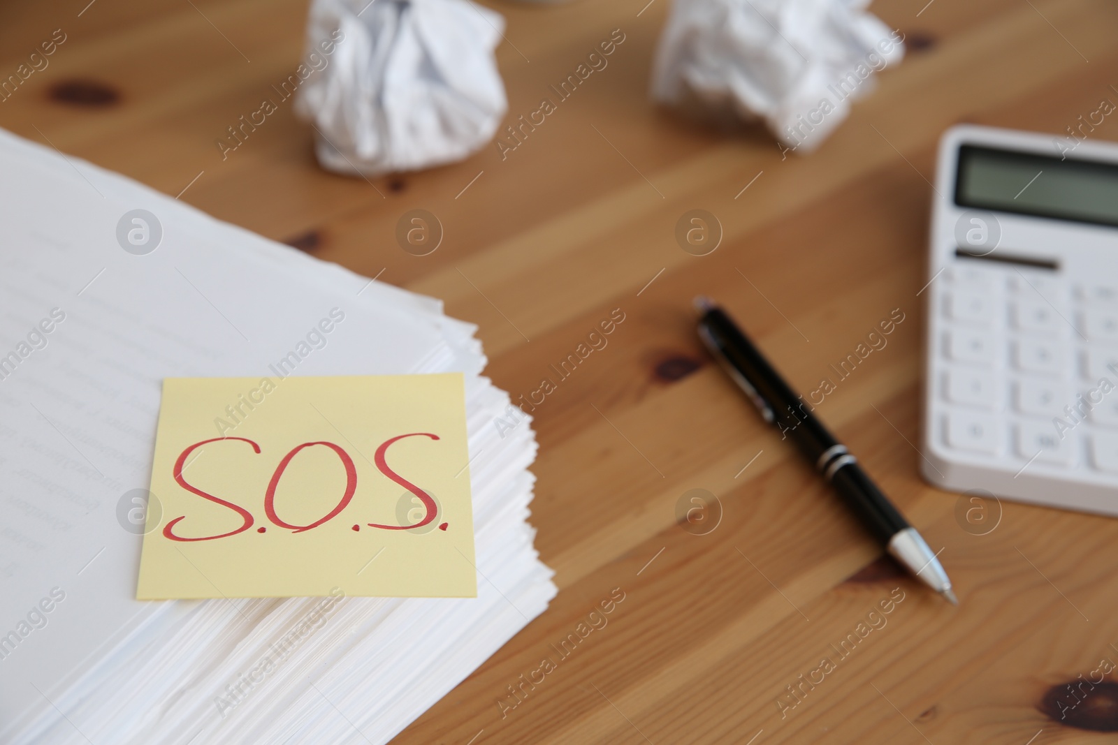 Photo of Note with word SOS and stationery on wooden table at workplace, closeup