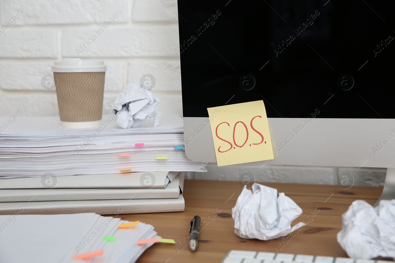 Photo of Note with word SOS and stationery on computer at workplace