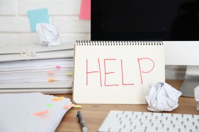 Photo of Notebook with word Help, computer and stationery on wooden table at workplace