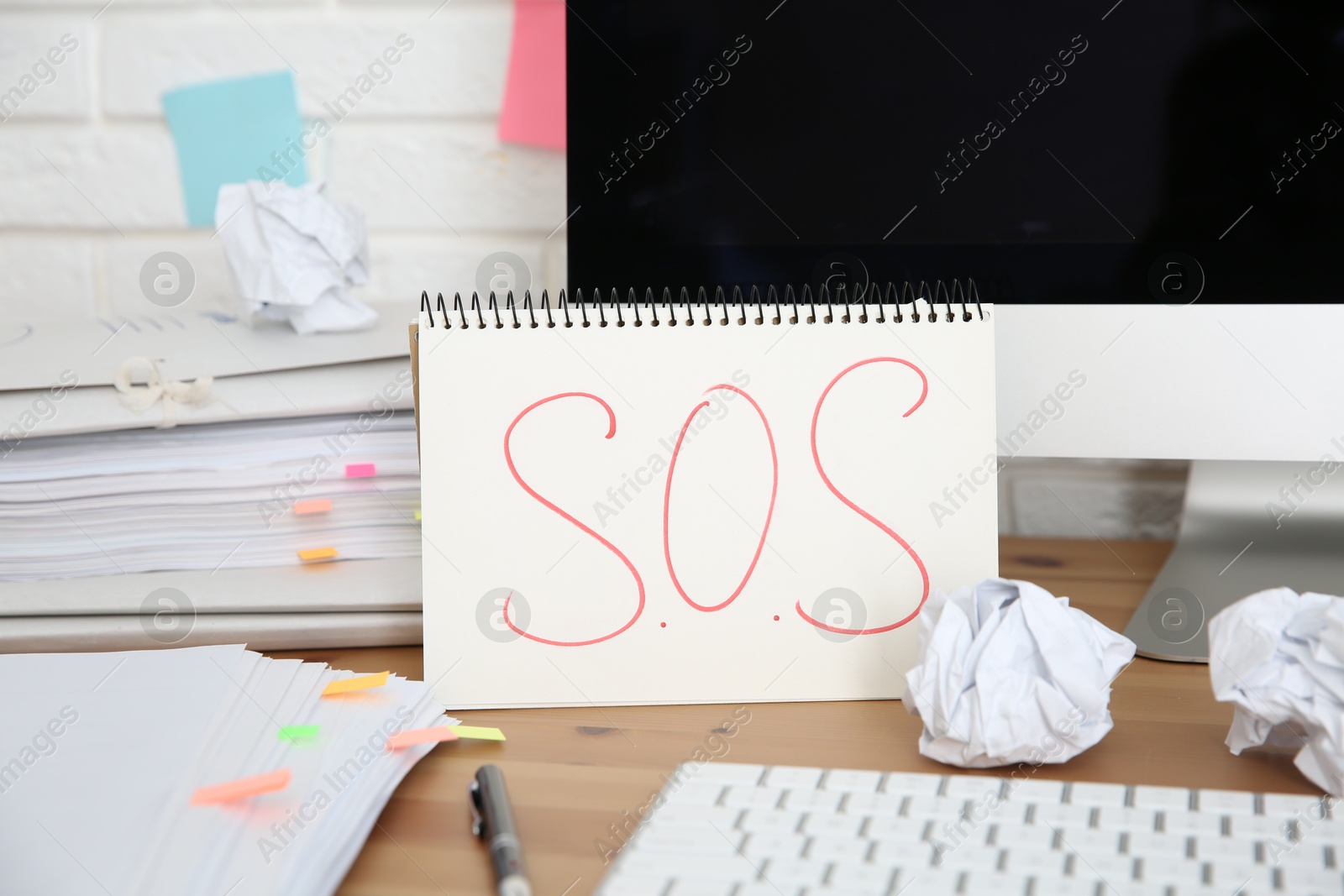 Photo of Notebook with word SOS, computer and stationery on wooden table at workplace