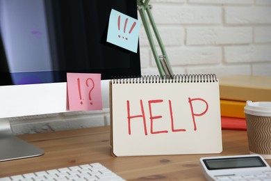 Photo of Notebook with word Help, computer and stationery on wooden table at workplace