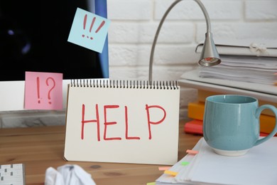 Photo of Notebook with word Help, computer and stationery on wooden table at workplace