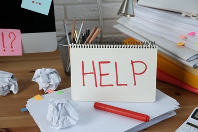 Photo of Notebook with word Help, computer and stationery on wooden table at workplace