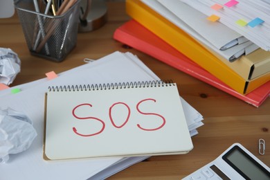 Photo of Notebook with word SOS and stationery on wooden table at workplace