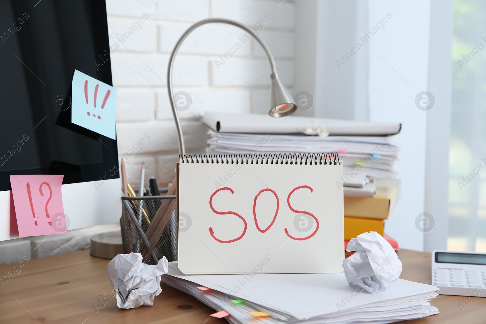 Photo of Notebook with word SOS and stationery on wooden table at workplace