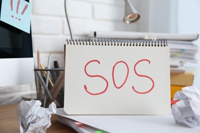 Photo of Notebook with word SOS and stationery on wooden table at workplace