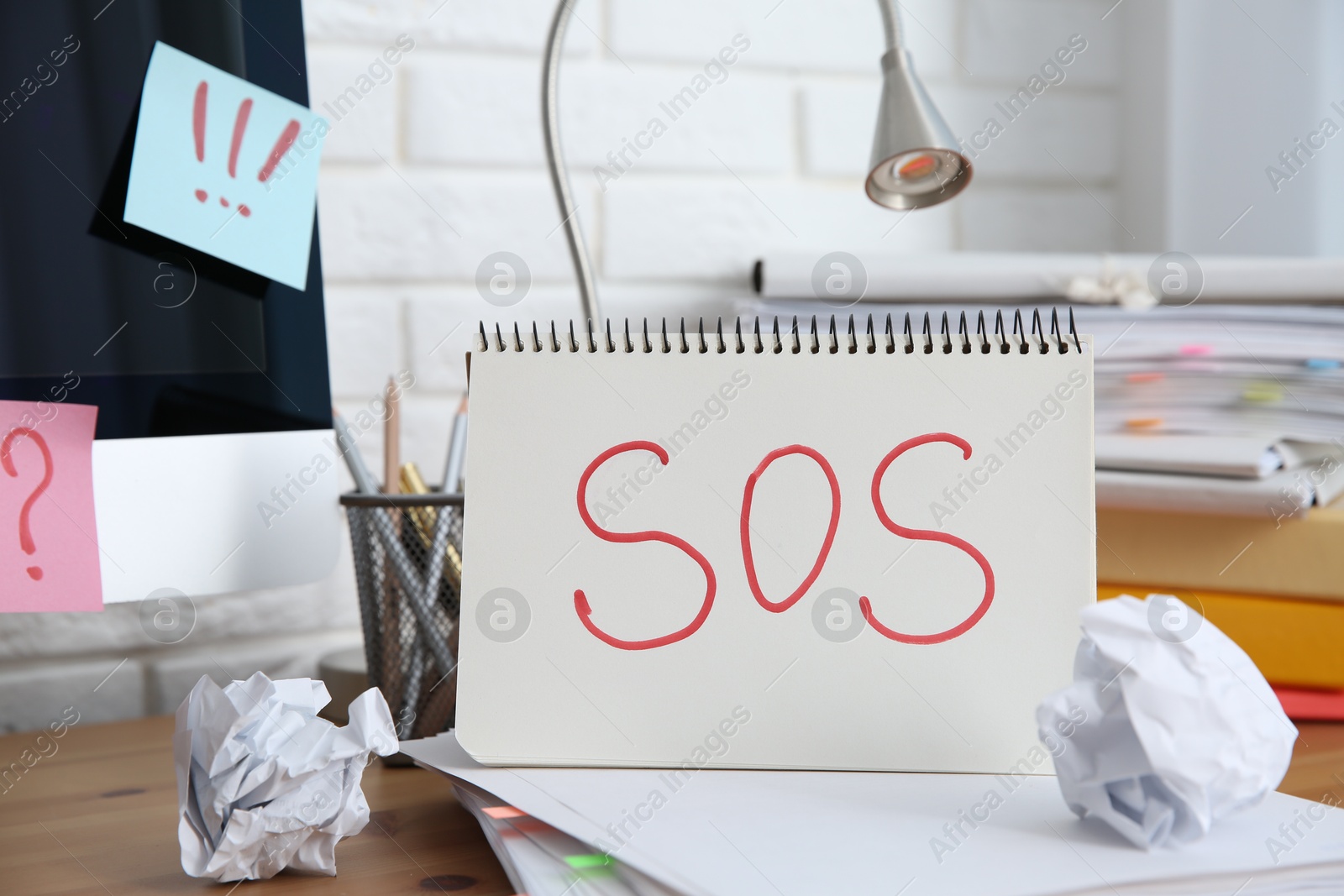 Photo of Notebook with word SOS and stationery on wooden table at workplace