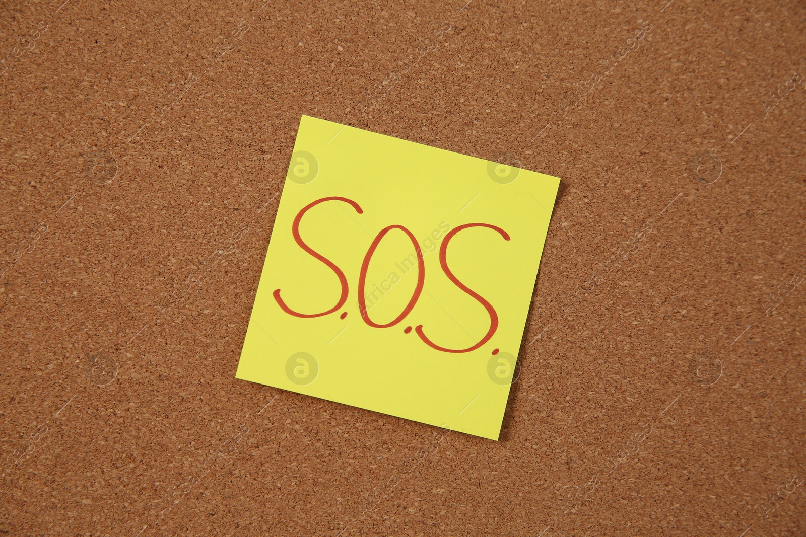 Photo of Note with word SOS and stationery on cork board, closeup