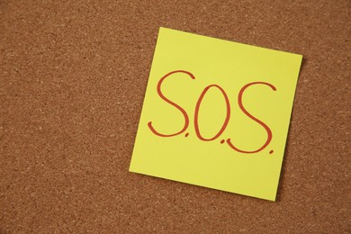 Photo of Note with word SOS and stationery on cork board, closeup