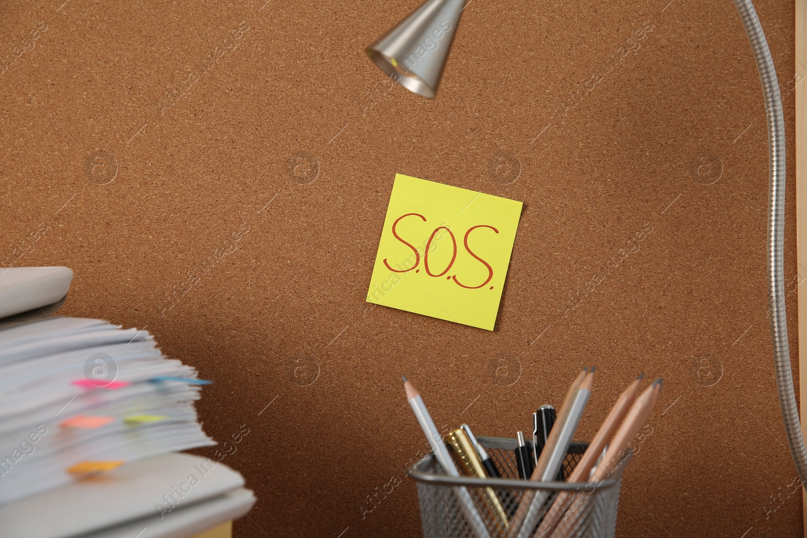 Photo of Note with word SOS and stationery on cork board