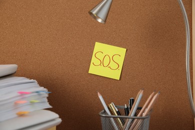 Photo of Note with word SOS and stationery on cork board