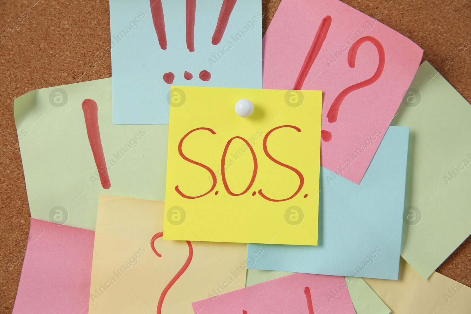 Photo of Notes with word SOS and symbols on cork board, closeup