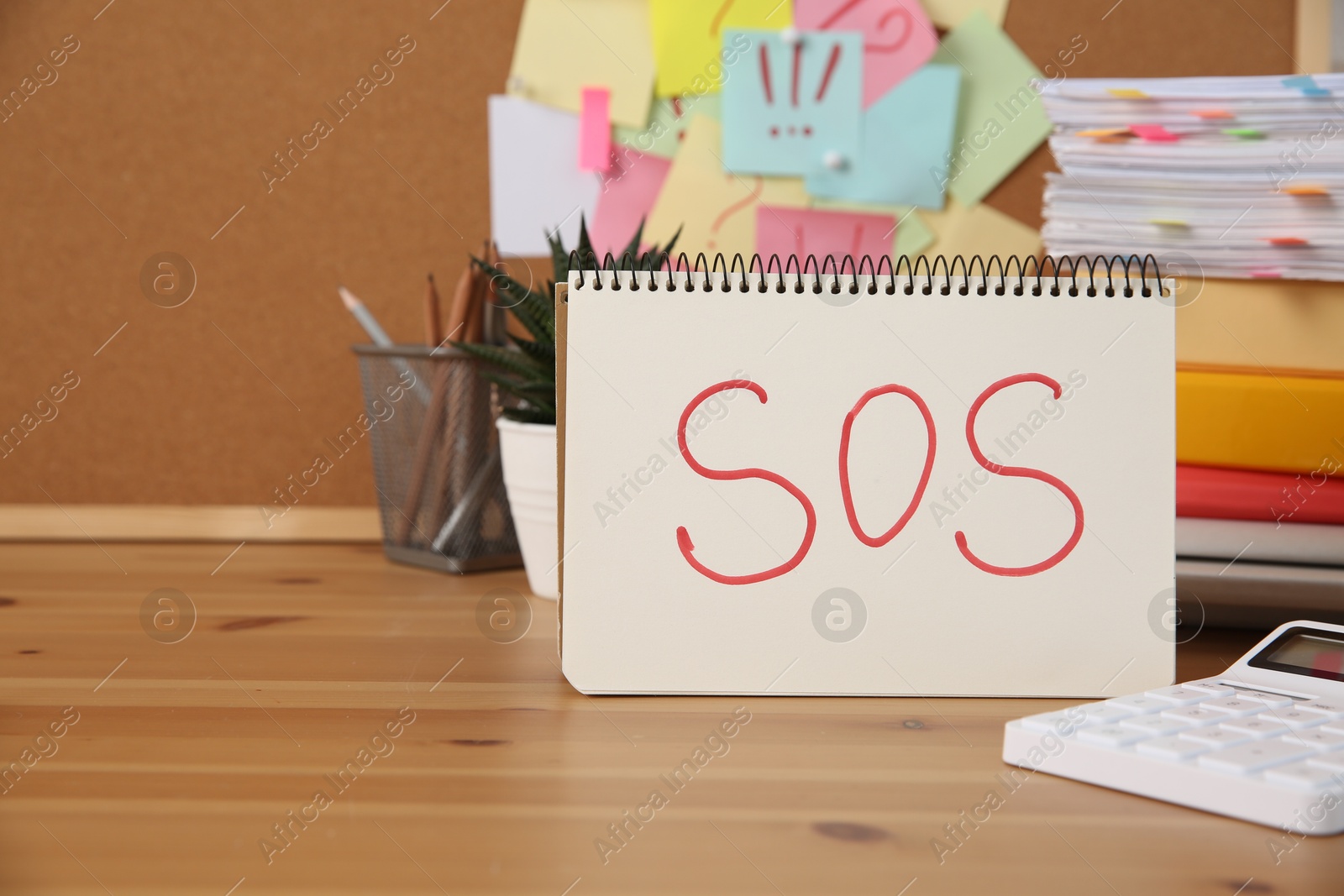 Photo of Notebook with word SOS and stationery on wooden table at workplace, space for text